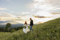 A group of five people, four women in gold dresses and a man in a dark suit, smile while holding flower bouquets. Captured by a Colorado Photographer, they are outdoors with trees in the background and sunlight filtering through.