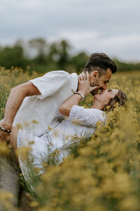 Couple s'embrassant dans un champ fleuri vert et jaune, capturés par Laura, photographe couple en Vendée.