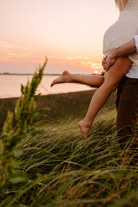 Groom lifting bride during engagement session in an field near the ocean
