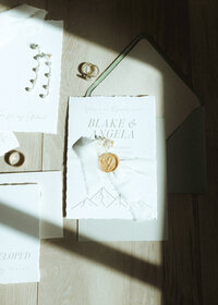 Deckled edge wedding invitation suite with mountain illustration, shot in natural light with flatlay styling in a bridal suite