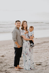 man and woman standing on the beach with their baby