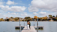 bride and groom hug at the end of a pier, in front of a lake in albert lea, mn