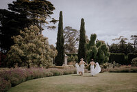 Two brides running across a lawn in a manicured garden