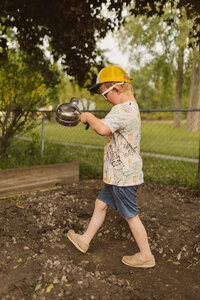 boy marches with pot and ladle acting as if he is a drummer in a marching band in the backyard mud kitchen