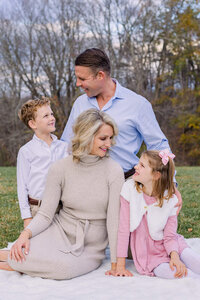 A family of four smiling at each other at a park in Fairfax County.