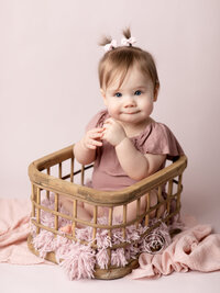 one year old girl sitting in basket for studio portraits