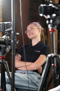 A smiling Storyteller team member sits behind a camera enjoying her job of filming a project.