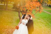 bride and groom kissing in front of an autumn tree