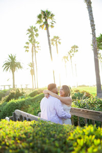 engaged couple smile on a bridge above the beach