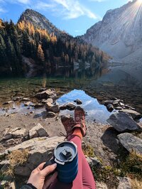 POV shot of coffee mug and legs extended in front of Washington Alpine Lake