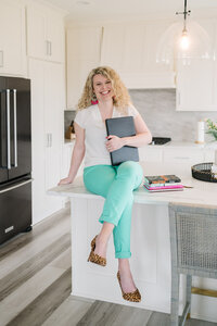 Katie Johnson sitting on kitchen counter holding portfolio folder