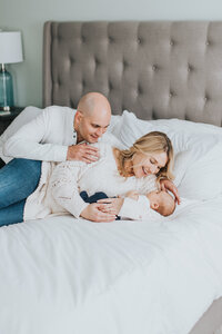Couple lays together on bed with newborn baby boy during lifestyle newborn session in Raleigh NC