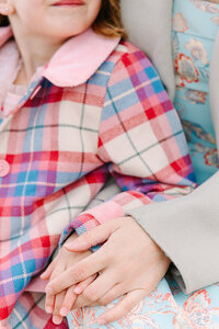 Close-up of daughter sitting on her mother’s lap, both wearing colorful jackets during a joyful mother-daughter photoshoot near the Eiffel Tower and Tuileries Garden in Paris.