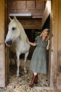 Leiko standing under a wooden barn in a soft green dress, embodying warmth and welcome