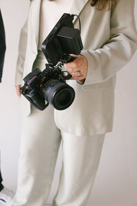 A poised woman elegantly holds a camera, ready to capture the world through her artistic lens