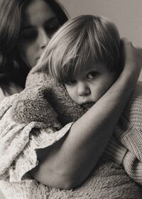 A young child snuggled up on their mother while holding their teddy bear.