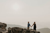 girl and guy standing on top of a mountain looking away from each other