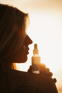 Luxury skincare brand photography featuring a woman holding a self-tanning facial serum, illuminated by golden sunset light. Storytelling and cinematic brand photography for beauty and wellness brands, captured on the Sunshine Coast.