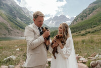 A wedding couple holds their two dogs in front of Maroon Bells in Aspen, Colorado.
