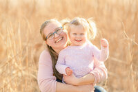 Mom with glasses hugging her toddler daughter both are wearing soft pink
