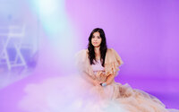 Whimsical fashion portrait of a woman in soft tulle gown, sitting in studio with purple haze – styled photo by Mewphotovideo