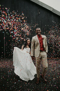 A bride and groom walk through a confetti tunnel at The Giraffe Shed.