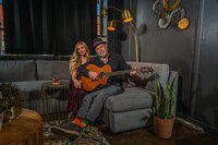 Two people sitting on a couch while one holds a guitar 