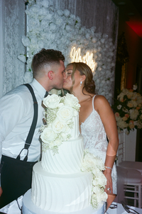 Couple kissing before cutting their three-tier floral wedding cake | SushDigitalMedia