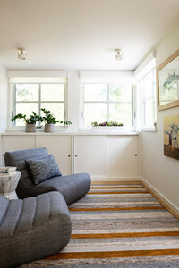 Interior decorators in Boston designed a modern reading nook at a new build home in Hingham, Massachusetts, featuring an orange and grey striped rug, grey chairs, and custom cabinets to hide kids’ books.