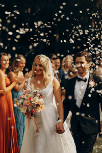 Bride and groom walking joyfully down the aisle with confetti being thrown, captured by a wedding photographer Sunshine Coast.
