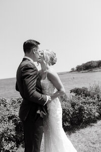 Photo of bride and groom kissing and holding hands while standing outside taken by Maine wedding photography