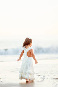 Young girl running playfully along the shore in Avila Beach during a session with Fresno, CA family photographer One Good Shot