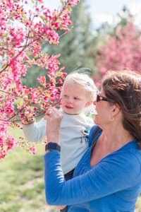 A grandma holds her grandchild up to show her the spring blossoms by Laramee Love Photography