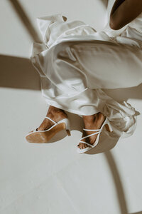 close up of woman's legs in white slip dress wearing white heels