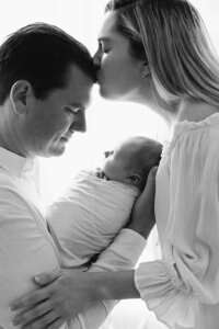 pregnant woman standing in a white gown, in a forest setting holding her pregnant belly looking down in awe.