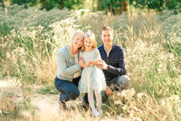 Family crouching down and hugging their young daughter ina  field of yellow grass