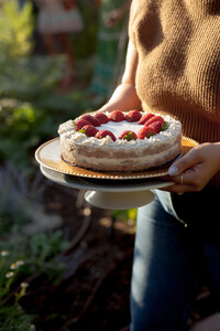 Woman holding a cakestand with a cake with strawberries on top on