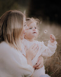 Mother holds daughter in her arms while they snuggle together, bumping noses