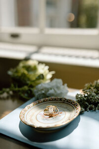 Wedding rings displayed on a vintage dish by the window