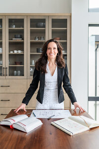 Professional architect wearing black blazer standing at head of table with papers in front looking at camera.