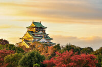 Traditional Japanese castle surrounded by colorful autumn trees under a warm, golden sky.