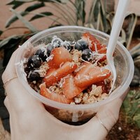 Brand photo of a hand holding an acai bowl