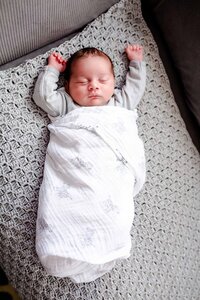 Newborn baby asleep on a couch with his arms over his head