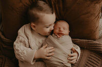 a big brother holding his little brother as he put his nose on his cheek in a newborn session