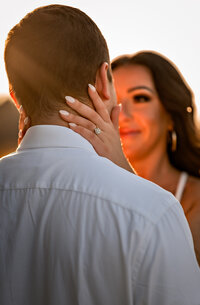 A couple looks at eachother during an enegagement session at sunset while the ring is shining