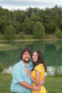 Couple hug and laugh while standing next to a lake in the summer