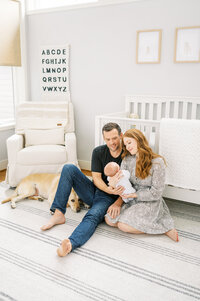 Couple holds and smiles at baby boy  on nursery floor in raleigh nc during newborn session with Worth Capturing Photography