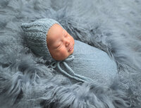 Studio-like newborn photo session of baby boy wrapped in light blue and sleeping on a matching fur. Image captured by Beth Benecki of E. Benecki Photography.
