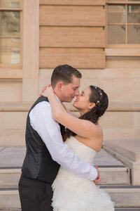 Bride and groom lean in an almost kiss on steps of building