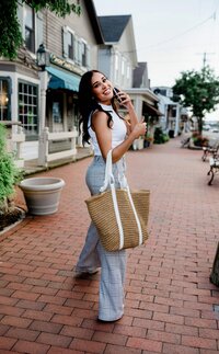 celebrity lifestyle shoot nail tech with a rattan tote bag on her arm while holding a phone up her ear
